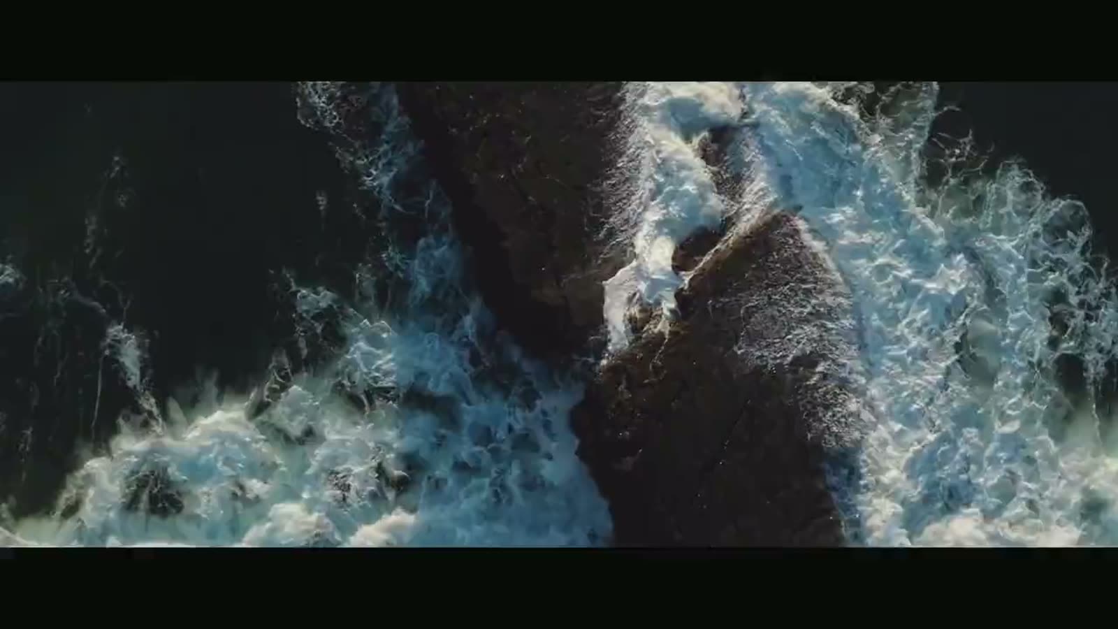 Waves breaking over dark rocks, seen from above, from the film Still Out.